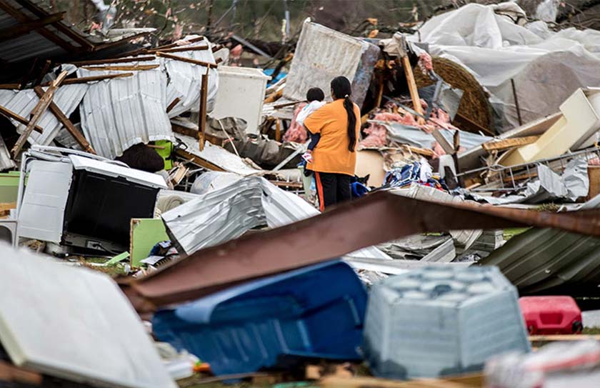 A woman holds a child while walking through a farm that was damaged by a tornado.