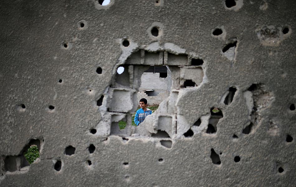 Seorang budak lelaki Palestin kelihatan melalui dinding dipenuhi bekas tembakan dari bangunan yang telah musnah semasa 50 hari perang antara Israel dan militan Hamas pada musim panas tahun 2014, di Bandar Gaza, 14 Januari 2016. AFP / MOHAMMED ABED Seorang budak lelaki Palestin kelihatan melalui dinding dipenuhi bekas tembakan dari bangunan yang telah musnah semasa 50 hari perang antara Israel dan militan Hamas pada musim panas tahun 2014, di Bandar Gaza, 14 Januari 2016. AFP / MOHAMMED ABED