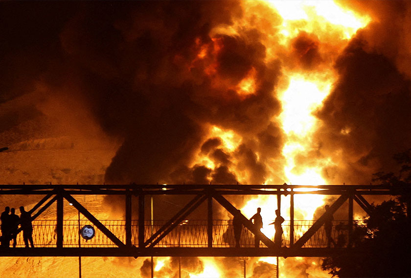 People watch from a bridge as flames from an Israeli attack rise from Sharan Oil depot, following Israeli strikes on Iran, in Tehran, Iran, June 15, 2025. - Majid Asgaripour/WANA (West Asia News Agency) via REUTERS